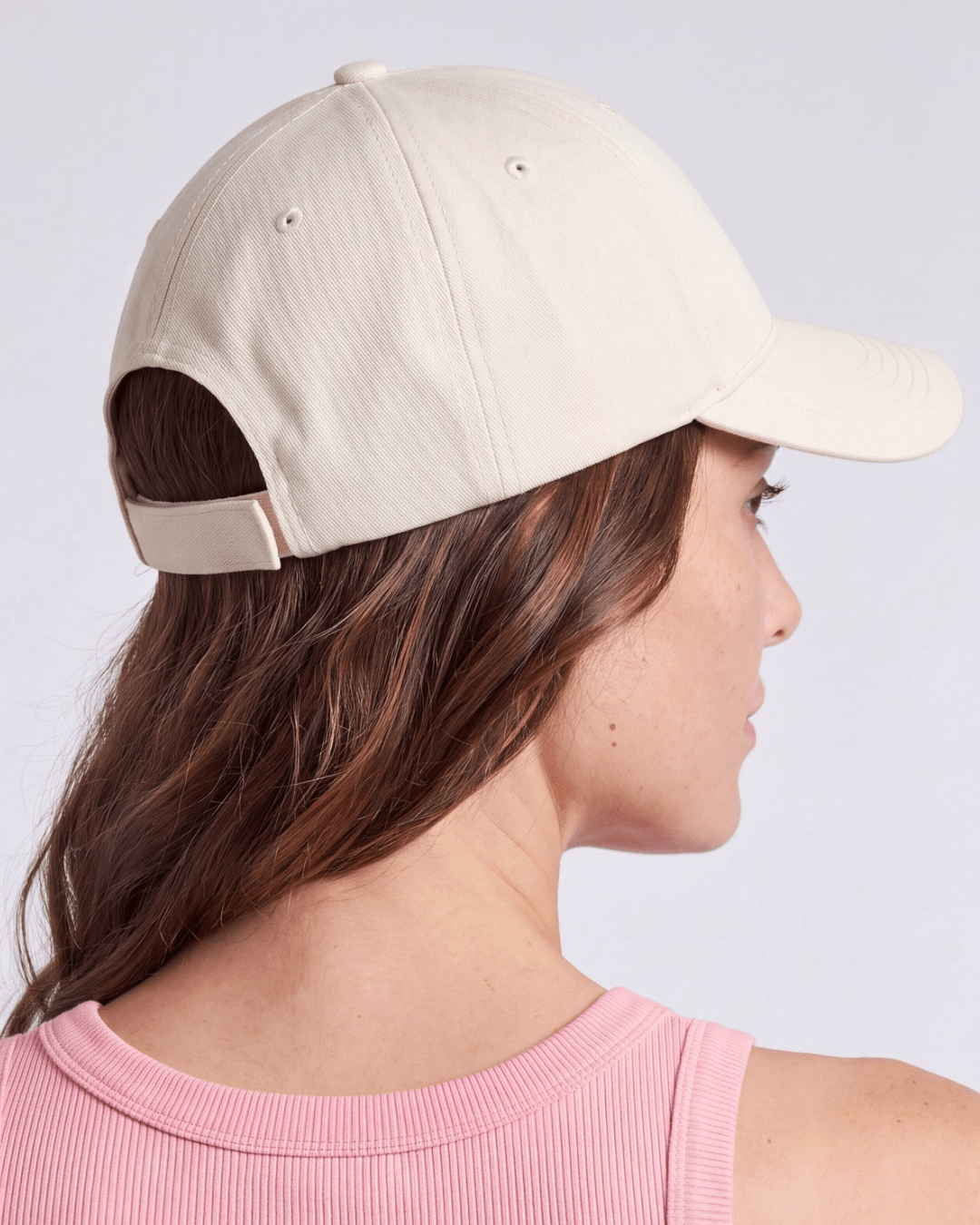Back of the cream cap, showing the fabric strap adjuster and the open gap above it for hair
